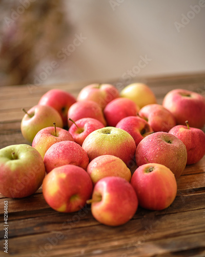 Lots of red apples are lying on a wooden table in the bright sunlight