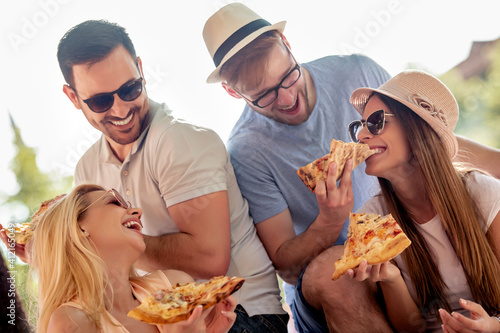 Group of friends eat pizza outdoors