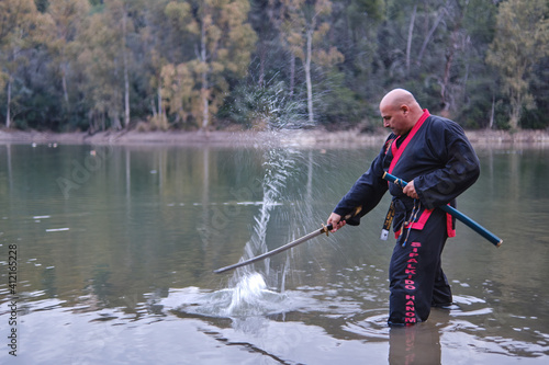 Sipalkido master hitting the water with katana in a lake with black and red uniform