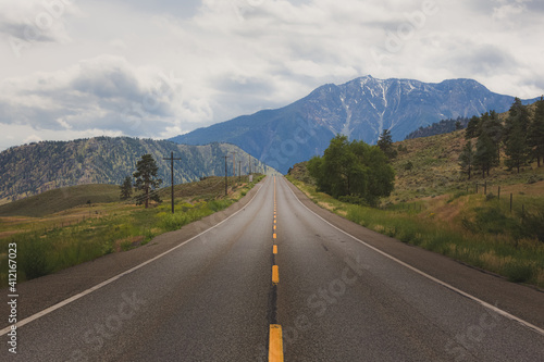 A wide open empty road straight ahead towards the mountain landscape on Highway 3 in the Similkameen Valley outside of Cawston, British Columbia, Canada.