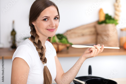 Young woman is cooking in a kitchen. Housewife is tasting the soup by wooden spoon
