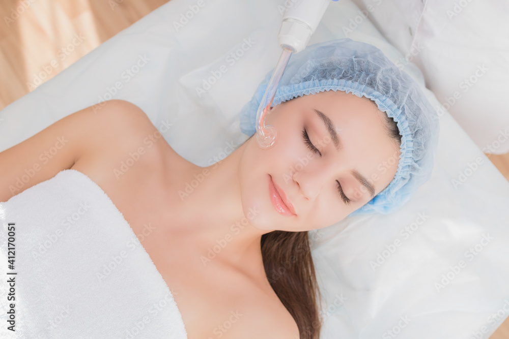Beautiful young woman receiving darsonval procedure electric massage at beauty salon. Hardware cosmetology. Selective focus. Beautiful young woman receiving darsonval procedure electric massage at beauty salon. Hardware cosmetology. Selective focus.