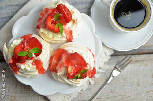 Small meringues with strawberries on a white plate on a wooden background