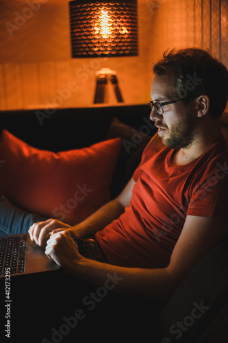 Portrait of attractive nerdy man is working late night on the computer in living room in home office photo