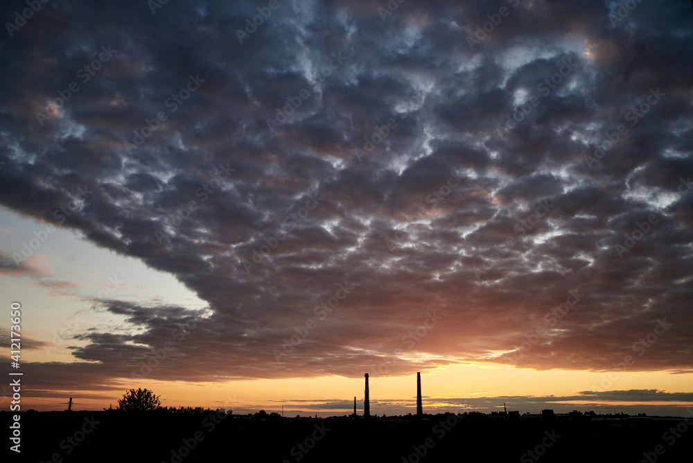 Beautiful city view at sunset. Industrial town landscape with setting sun and purple yellow pink blue cloudy sky.