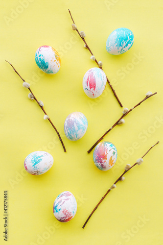 easter eggs abstractly painted in different colors and willow branches on a yellow background, vertical frame