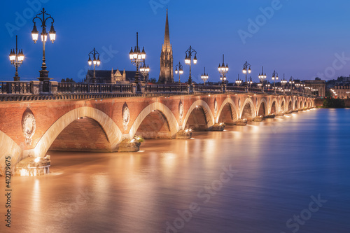 The historic Pont de Perre illuminated at night over the River Gardonne in Bordeaux, France with Bordeaux Cathedral in the background. photo