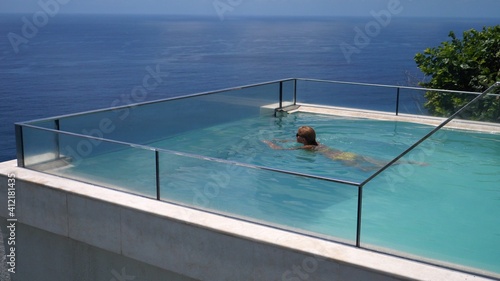 Happy middle aged woman swimming in an infinity pool overlooking an ocean. Luxurious resorts concept. photo