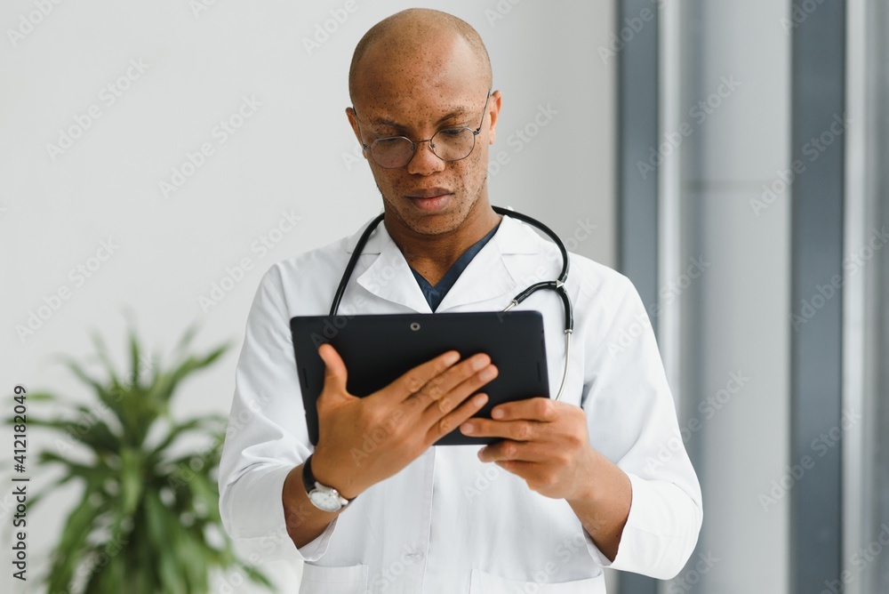 Mature african doctor using digital tablet in corridor . Portrait of confident male doctor using tablet computer in clinic with copy space. Successful smiling doctor in labcoat wearing stethoscope. Mature african doctor using digital tablet in corridor . Portrait of confident male doctor using tablet computer in clinic with copy space. Successful smiling doctor in labcoat wearing stethoscope.