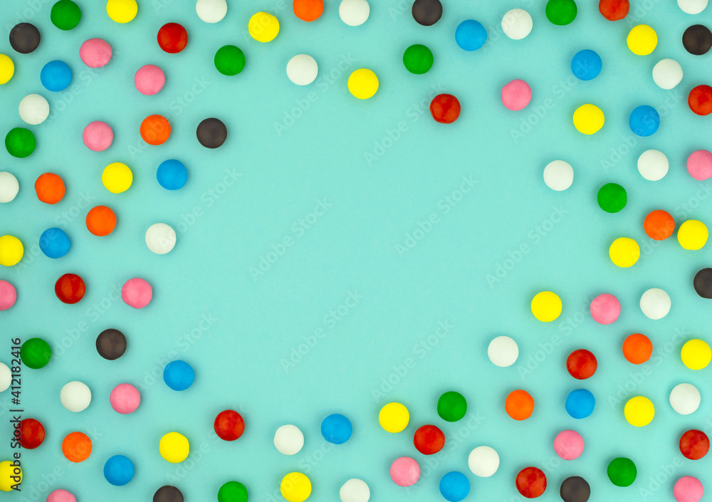 Multicolored candies frame on blue background. Chocolate sweets in colored glaze. Birthday greetings. Congratulations on holiday. Festive background for your text