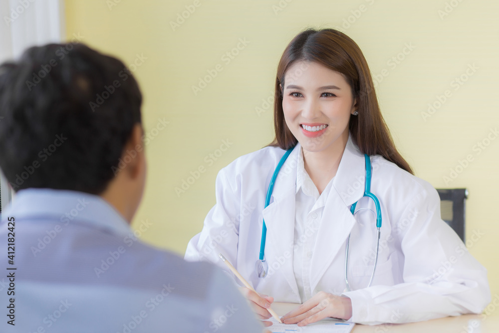 A beautiful Asian female doctor smiled and asked about the symptoms. Stay at the hospital wearing a white robe and stethoscope A beautiful Asian female doctor smiled and asked about the symptoms. Stay at the hospital wearing a white robe and stethoscope