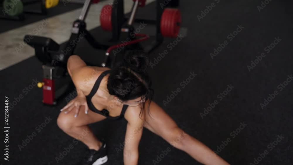 A beautiful woman warms up before training in the gym. She is dressed in dark sportswear A beautiful woman warms up before training in the gym. She is dressed in dark sportswear