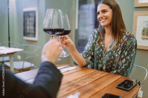 Young woman having a romantic celebrative wine toast. Couple clinking with wineglasses in a bistrot restaurant bar. photo