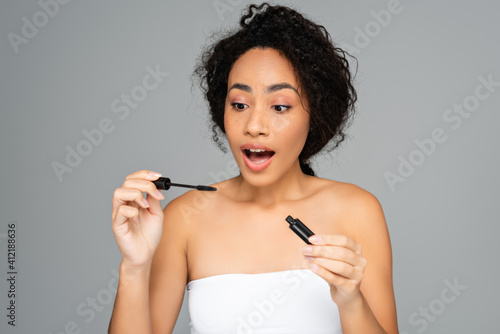 Excited african american woman holding mascara isolated on grey