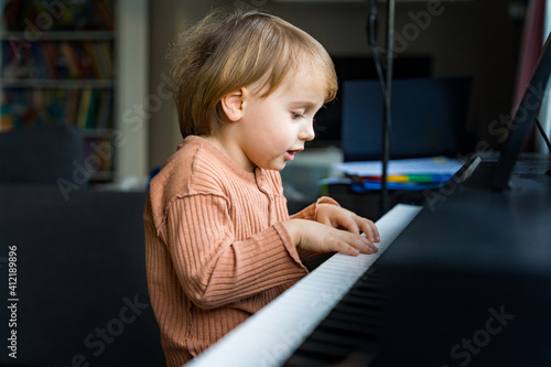 Close up portrait of adorable little toddler boy. Smiling child playing piano at home. Kid learning  play music. Early development.