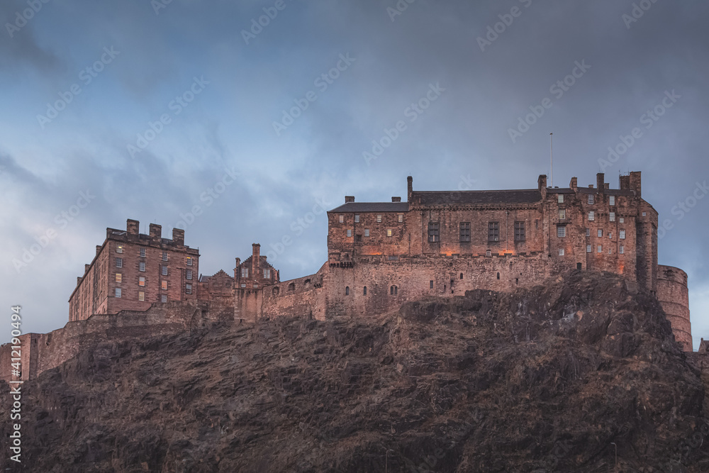 The historic Edinburgh Castle perched atop Castlehill against a moody backdrop on a dark night in Scotland.