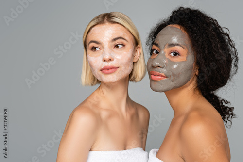 Young multicultural women with facial masks standing isolated on grey photo
