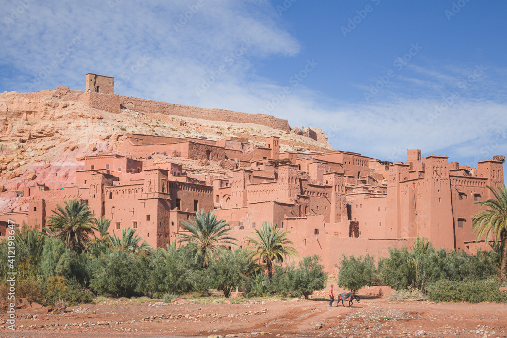Scenic view of oasis old town Ait Benhaddou, Morocco a historic fortified village, noted for its ancient clay earthen architecture with a distant local Moroccan man and his pack mule.