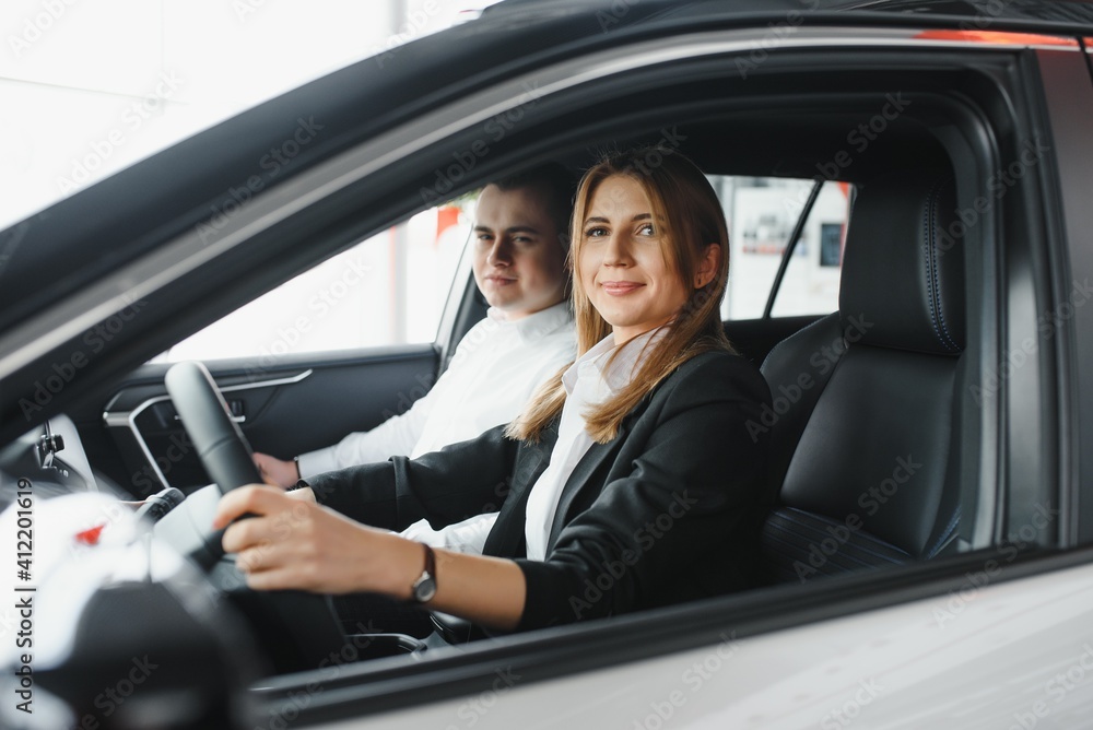 Visiting car dealership. Beautiful couple is looking at camera and smiling while sitting in their new car Visiting car dealership. Beautiful couple is looking at camera and smiling while sitting in their new car