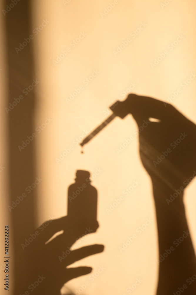 Hand holding a dropper with oil and a bottle. Shadow, silhouette.  - obrazy, fototapety, plakaty 