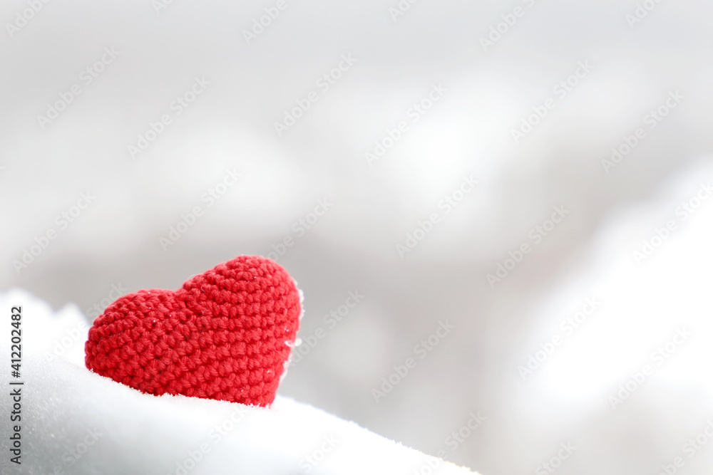 Fototapeta premium Valentine heart in the snow, background for greeting card. Red knitted symbol of romantic love in winter forest
