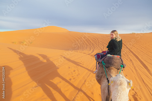 A young blonde female tourist on a camelback excursion along the desert sand dunes of Erg Chebbi near the village of Merzouga in southeastern Morocco. photo