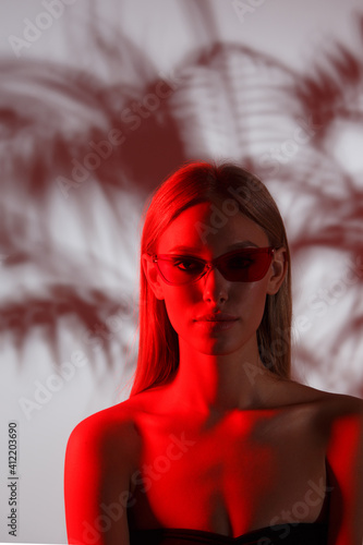 Cinematic portrait of young girl in red neon light. Wearing modern sunglasses