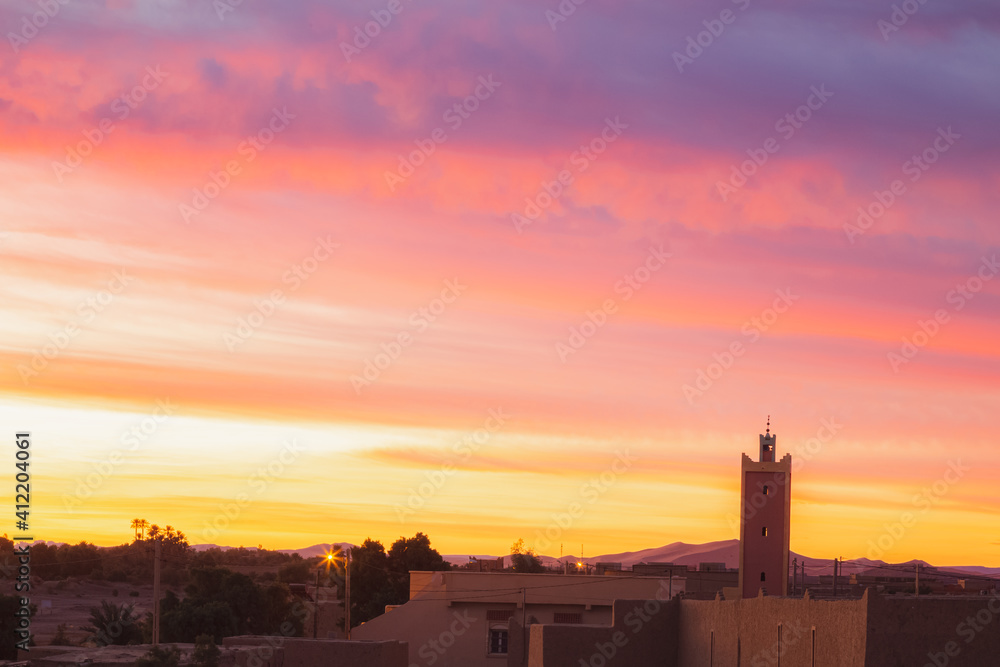 A vibrant colourful sunrise or sunset over the village of Merzouga, the gateway to the Erg Chebbi desert dunes in Morocco.