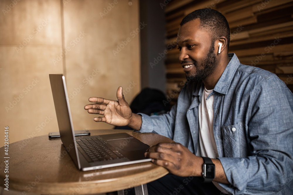 Friendly African American using a laptop, looking at the screen, chatting with colleagues on a social network, reading good news via email. Business young man negotiates a working plan. Friendly African American using a laptop, looking at the screen, chatting with colleagues on a social network, reading good news via email. Business young man negotiates a working plan.