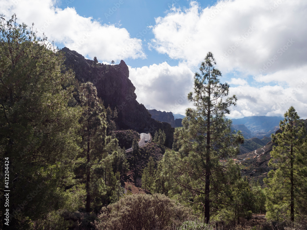 Scenic view of amazing landscape from path to Roque Nublo rock formation with winding road, mountains, green pine trees and blue sky, white clouds. Gran Canaria, Canary Islands, Spain