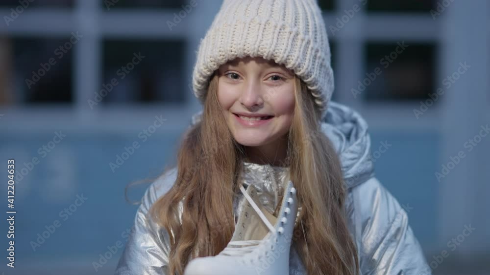 Close-up of charming happy girl admiring new ice skates standing outdoors. Portrait of joyful Caucasian cute kid looking at camera smiling holding gliding equipment. Winter sport and childhood. Close-up of charming happy girl admiring new ice skates standing outdoors. Portrait of joyful Caucasian cute kid looking at camera smiling holding gliding equipment. Winter sport and childhood.