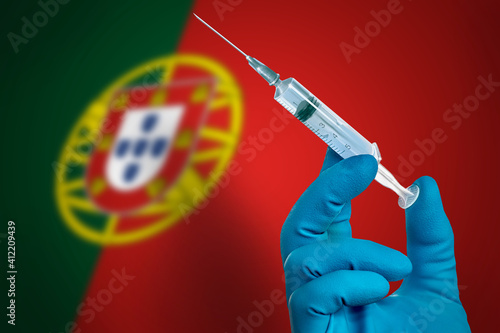 COVID-19 Pandemic Coronavirus concept .Doctor's hand in gloves with vaccine in a syringe for the treatment of the COVID-19 on the background of the flag of Portugal