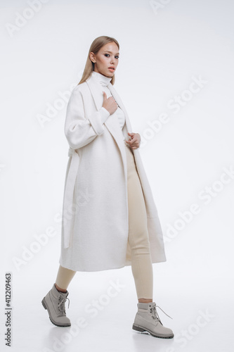 young fashionable beautiful girl in a trendy white coat posing on a white background