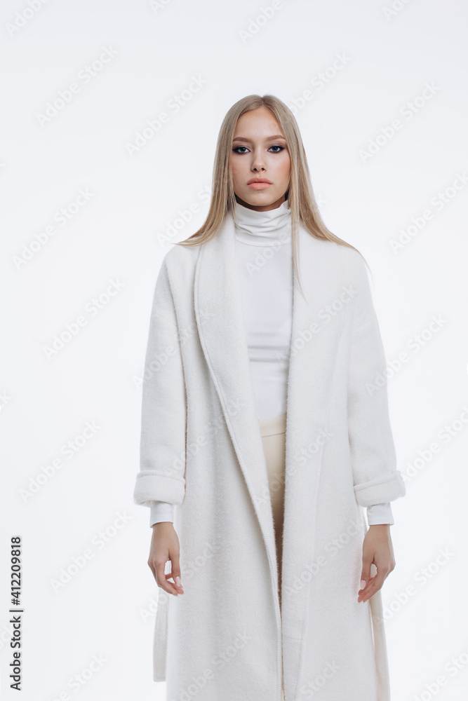 Fototapeta premium young fashionable beautiful girl in a trendy white coat posing on a white background