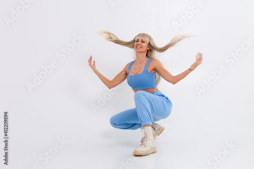Fototapeta Naklejka Na Ścianę i Meble -  Fashion portrait of young happy blonde woman with long gorgeous straight hair and bangs in the studio on a white background. The girl is dressed in a trendy blue suit, warm pants and a top