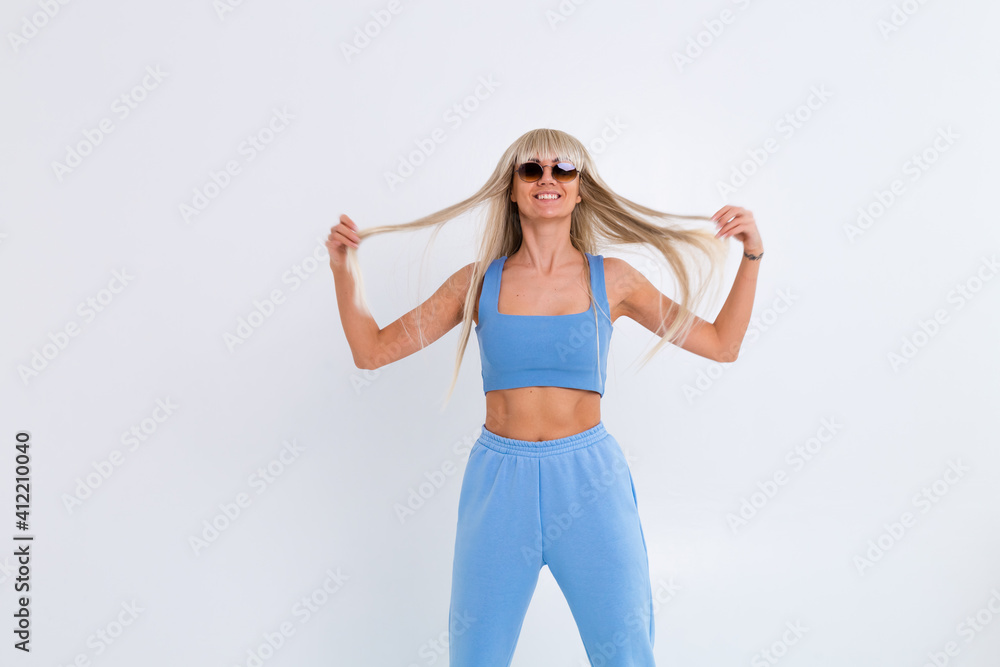 Fashion portrait of young happy blonde woman with long gorgeous straight hair and bangs in the studio on a white background. The girl is dressed in a trendy blue suit, warm pants and a top Fashion portrait of young happy blonde woman with long gorgeous straight hair and bangs in the studio on a white background. The girl is dressed in a trendy blue suit, warm pants and a top