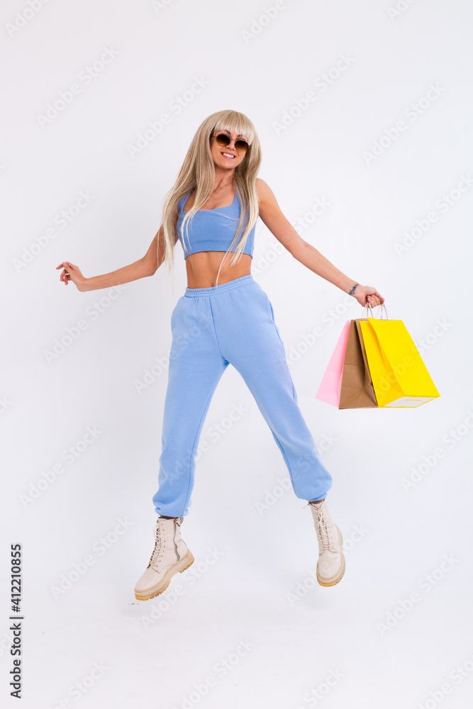 Fashion portrait of young happy blonde woman with long gorgeous straight hair with colorful shopping bags in the studio on a white background.