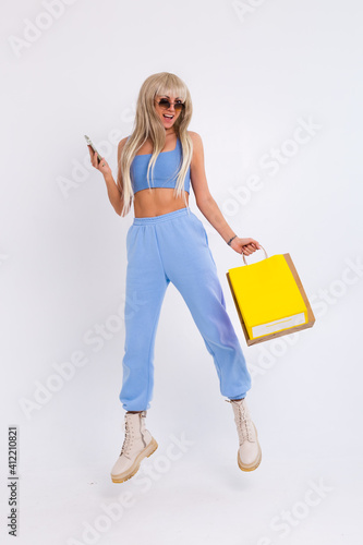 Fashion portrait of young happy blonde woman with long gorgeous straight hair hold colorful shopping bags and mobile phone in the studio on a white background.