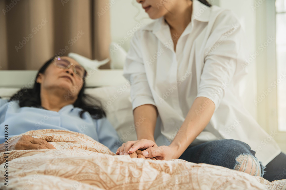 Obraz premium A young hand touches and holds an old wrinkled hand. Worried woman holding and gently stroking hand of his sick mother giving support.Visitor holding hand of female patient in hospital bed.