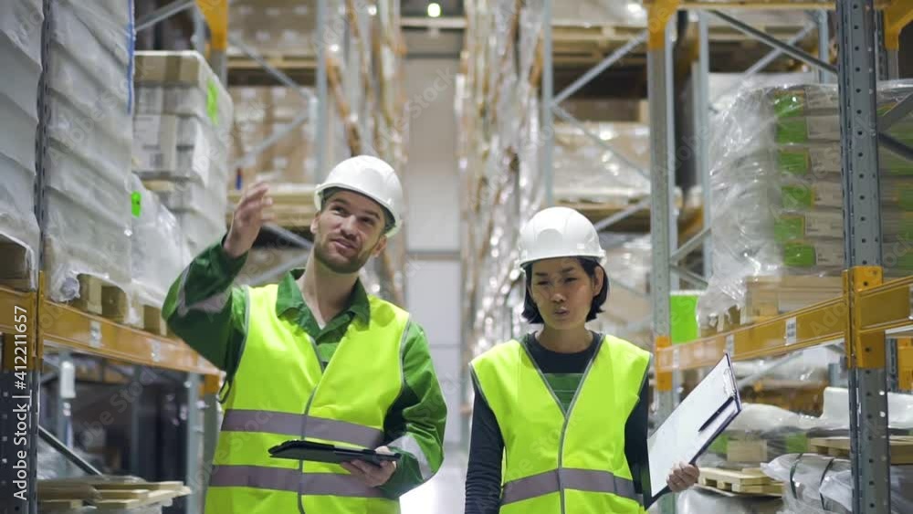 Two american employees are talking about work during working day at industrial warehouse. Front view of young man and woman having conversation and smiling while doing job on modern storehouse. People Two american employees are talking about work during working day at industrial warehouse. Front view of young man and woman having conversation and smiling while doing job on modern storehouse. People