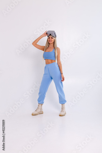 Studio photo of a young attractive woman in a warm blue fashionable suit wearing virtual reality glasses on a white background