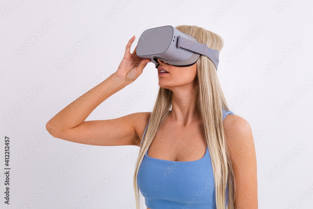 Studio photo of a young attractive woman in a warm blue fashionable suit wearing virtual reality glasses on a white background Studio photo of a young attractive woman in a warm blue fashionable suit wearing virtual reality glasses on a white background