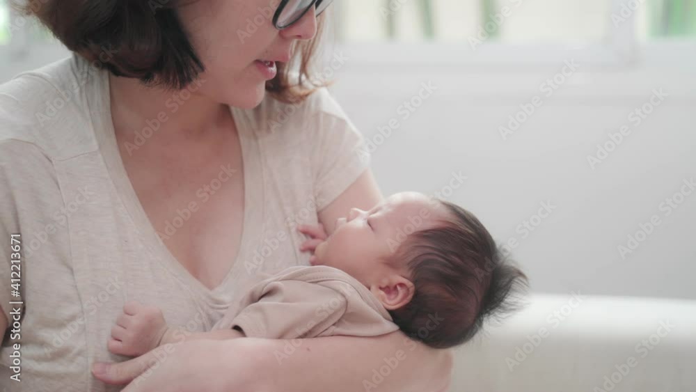 asian woman mother embracing baby on body looking at infant with love emotion. female parent holding and talking to sleeping daughter at home. asian woman mother embracing baby on body looking at infant with love emotion. female parent holding and talking to sleeping daughter at home.
