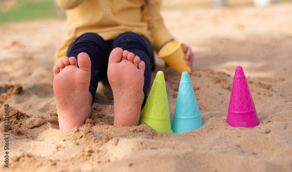 Little cute legs feet of child with molds for sand. Summer joy and play outdoor. Ice-cream molds different colours. Great vacation with children. Little cute legs feet of child with molds for sand. Summer joy and play outdoor. Ice-cream molds different colours. Great vacation with children.