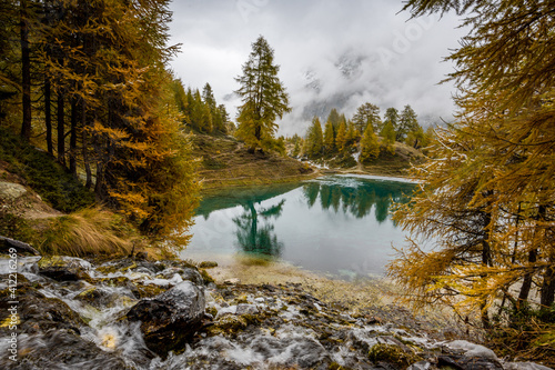 autumn creek with yellow larches and mountain lake in Valais photo