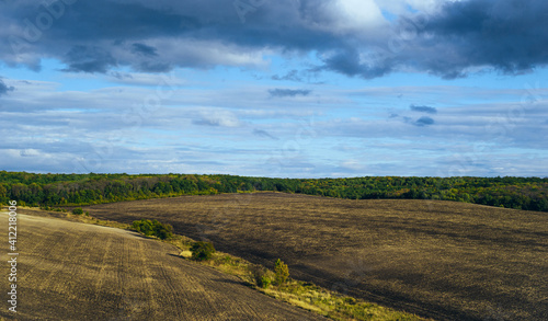 Field after harvesting, blck earth. The soil processed by a disk harrow. Cultivated land prepared for sowing. Hilly landscape with dramatic sky, field forest.