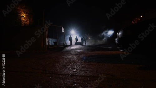 Wide shot of a group of men standing in the shadows in the night, dangerous criminals in smoke. Dangerous, urban scene. photo
