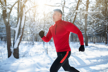 Senior athletic man in sportswear running at winter park, copy space. Seasonal outdoor sports and cold tempering concept
