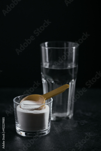 Collagen powder in bowl, glass of water and measure spoon on black background. Extra protein intake