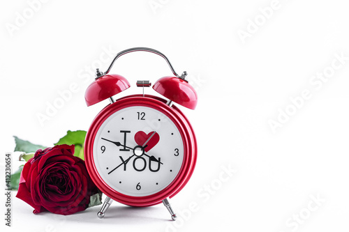 Red alarm clock with one rose on a white background. Greeting card for Valentine's Day. Copy space. photo